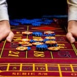 Man's Hands Beside Blue and Yellow Money Chips Laying on Red Casino Game Table