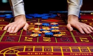 Man's Hands Beside Blue and Yellow Money Chips Laying on Red Casino Game Table