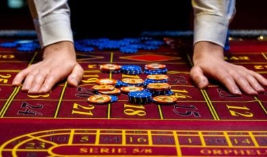 Man's Hands Beside Blue and Yellow Money Chips Laying on Red Casino Game Table