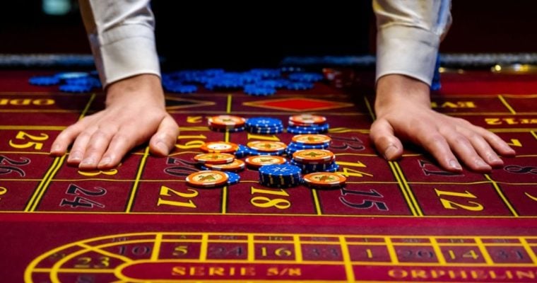Man's Hands Beside Blue and Yellow Money Chips Laying on Red Casino Game Table