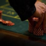 Man Touches Large Stack of Red and White Poker Chips on Green Game Table