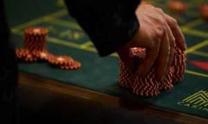 Man Touches Large Stack of Red and White Poker Chips on Green Game Table