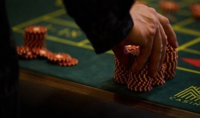 Man Touches Large Stack of Red and White Poker Chips on Green Game Table