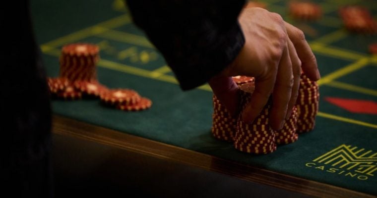 Man Touches Large Stack of Red and White Poker Chips on Green Game Table