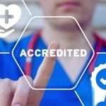 Hospital Nurse in Blue Garb Points to Digital Overlay of the Word Accredited in White Text