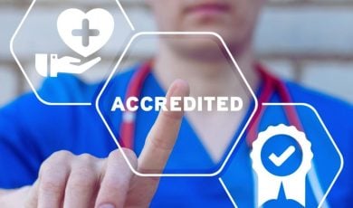 Hospital Nurse in Blue Garb Points to Digital Overlay of the Word Accredited in White Text