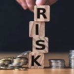 Finger Sits On Wood Blocks Spelling Risk In Between Silver Coins on Desk