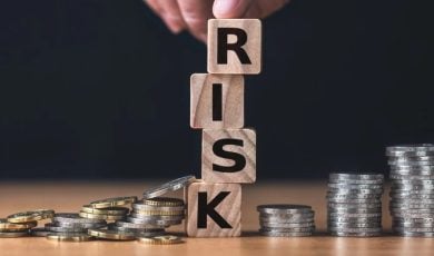 Finger Sits On Wood Blocks Spelling Risk In Between Silver Coins on Desk