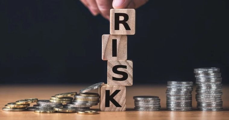 Finger Sits On Wood Blocks Spelling Risk In Between Silver Coins on Desk