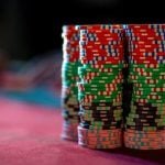 Stacks of Red, Green, Orange and Black Poker Chips Sit on Red Game Table with Blurred Background