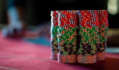 Stacks of Red, Green, Orange and Black Poker Chips Sit on Red Game Table with Blurred Background