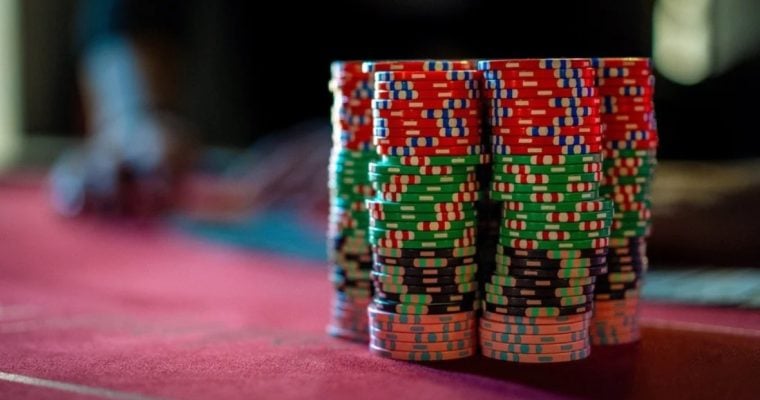 Stacks of Red, Green, Orange and Black Poker Chips Sit on Red Game Table with Blurred Background