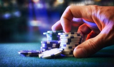 Man Touches Stacks of Blue and White Colored Poker Chips on Green Game Table