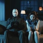 Man With Ski Mask Sits Next To Woman On Couch, Both Looking at Cell Phones