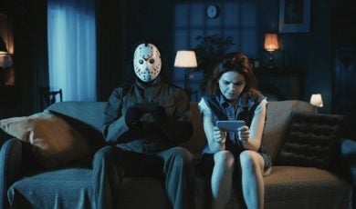 Man With Ski Mask Sits Next To Woman On Couch, Both Looking at Cell Phones
