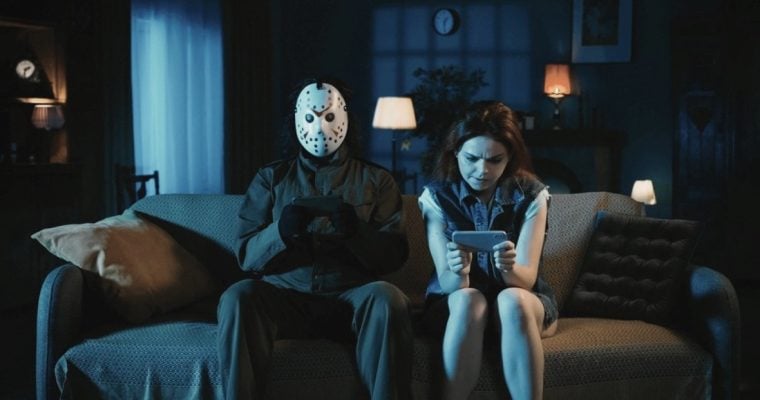 Man With Ski Mask Sits Next To Woman On Couch, Both Looking at Cell Phones