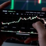 Man Uses Smartphone to Check Rising Financial Graph