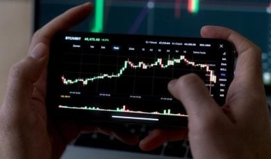 Man Uses Smartphone to Check Rising Financial Graph