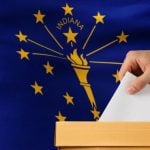 Indiana State Flag Sits Behind Ballot Box with Man Placing White Envelope Inside