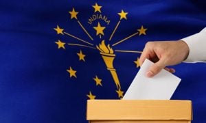 Indiana State Flag Sits Behind Ballot Box with Man Placing White Envelope Inside