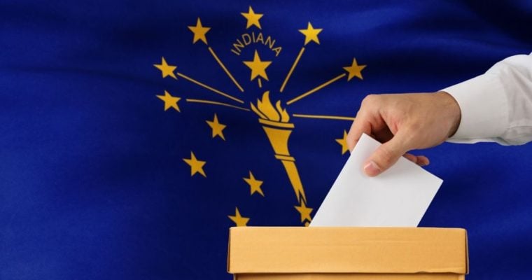Indiana State Flag Sits Behind Ballot Box with Man Placing White Envelope Inside
