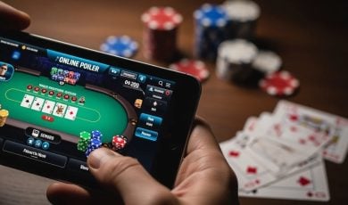Man Plays Online Poker with Smartphone and Poker Chips, Playing Cards on Table in Background