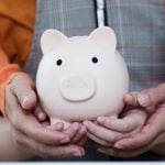 Adult Holds Child's Hands As They Hold Porcelain Piggy Bank