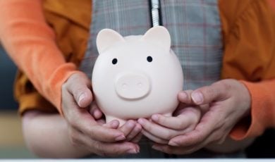 Adult Holds Child's Hands As They Hold Porcelain Piggy Bank