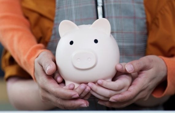 Adult Holds Child's Hands As They Hold Porcelain Piggy Bank