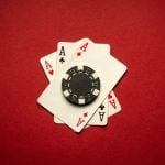 Black Poker Chip Sits on 3 Ace Playing Cards on Red Background
