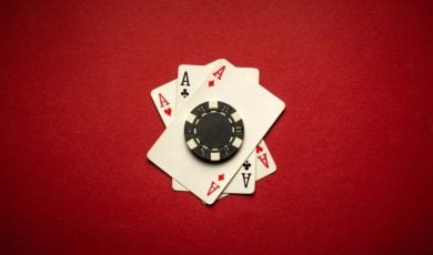 Black Poker Chip Sits on 3 Ace Playing Cards on Red Background