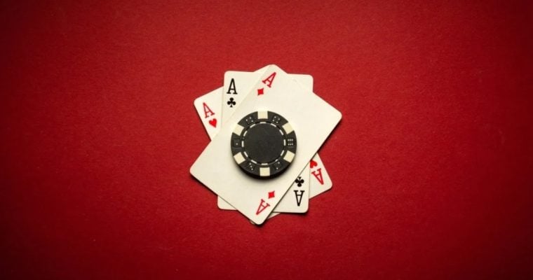 Black Poker Chip Sits on 3 Ace Playing Cards on Red Background