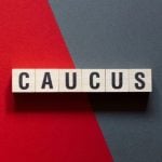 Red and Grey Split Background with Wooden Blocks Spelling Caucus