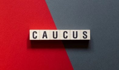 Red and Grey Split Background with Wooden Blocks Spelling Caucus
