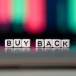 Buy Back Spelled Out in Tiny White Blocks Against Blurred Financial Graph in Background